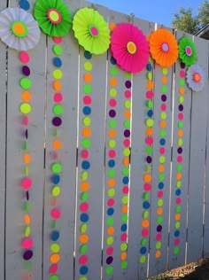 colorful paper flowers are hanging on the side of a white picket fence with rainbow dots