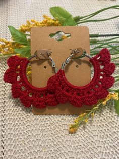 two red crocheted hoop earrings with metal hooks on top of a white table