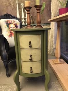 a green and white dresser with candles on it's top, next to a chair