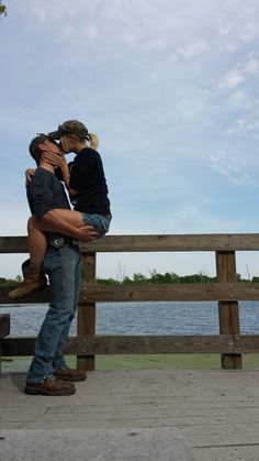 a man and woman are hugging on a bench by the water