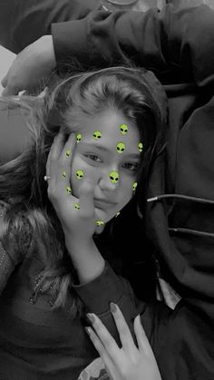 a girl with green smiley faces on her face is covering her eyes and looking at the camera