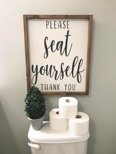 a toilet with two rolls of toilet paper on it and a sign that says please seat yourself thank you