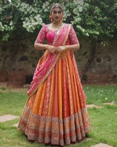 a woman in an orange and pink lehenga is posing for the camera with her hands on her hips