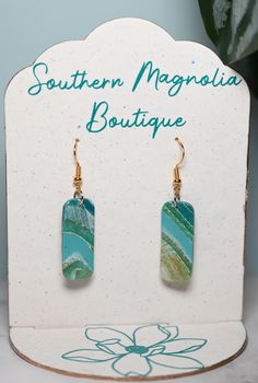 the earrings are on display in front of a white sign with blue and green designs