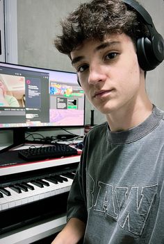 a young man wearing headphones sitting in front of a computer keyboard and monitor with music playing on it