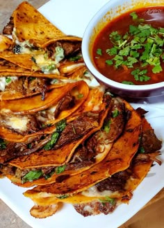 a white plate topped with nachos next to a bowl of salsa