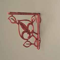 a red metal shelf with a flower design on it's side and a hook in the middle