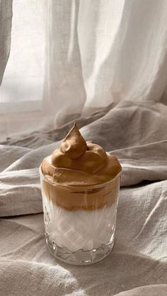 a glass jar filled with whipped cream on top of a bed next to a window