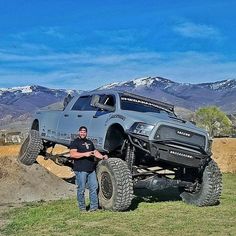 a man standing next to a large truck on top of a grass covered field with mountains in the background