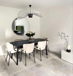 a dining room table with white chairs and a round mirror on the wall above it