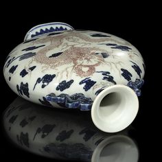 a white and blue vase sitting on top of a black table next to a cup