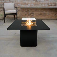 a fire pit sitting on top of a black table next to a chair and brick wall