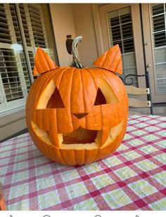 a pumpkin carved to look like a cat sitting on top of a checkered table cloth