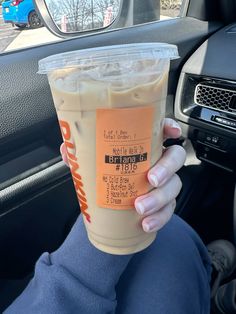 a person holding up a drink in their hand while sitting in the driver's seat