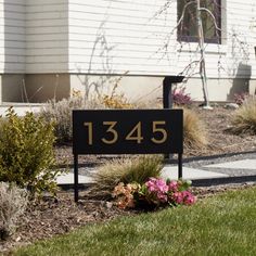 a black and gold address sign in front of a white house with flowers on the lawn