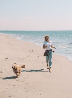 a woman is running on the beach with her dog while another runs along the shore