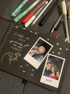 an open notebook with two photos and pens on the cover next to markers, crayons, and marker pens