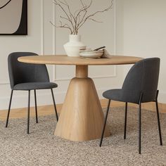 a dining table with two chairs and a vase on the top, in front of a white wall