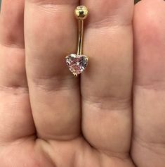 a person holding a gold ring with a pink heart shaped diamond in it's center