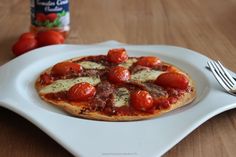 a small pizza on a white plate next to a fork and bottle of tomato sauce