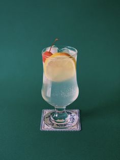 a glass filled with liquid and topped with an orange slice next to a coaster on a green surface