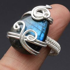 a wire wrapped ring with a blue stone on it's side, sitting on top of a finger