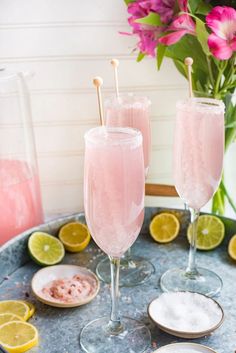 two glasses filled with pink lemonade sitting on top of a table next to plates and flowers