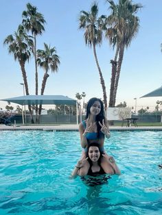 two women are sitting on the back of a woman in a pool with palm trees