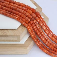 three strands of orange coral beads are on display in front of a wooden box and white background