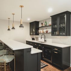 a modern kitchen with black cabinets and white counter tops, gold pendant lights and bar stools