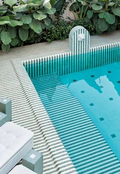 an empty swimming pool surrounded by greenery and white lounge chairs in front of it