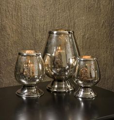 three silver goblets sitting on top of a black table next to a brown wall