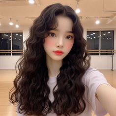 a woman with long dark curly hair is taking a selfie in an empty room