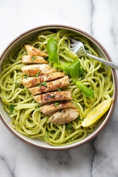 a bowl of pasta with chicken and pesto on the side next to a lemon wedge