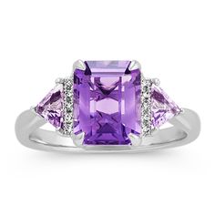 Ten round diamonds (approx. .05 carat TW) and two trillion shaped light purple amethyst (approx. .34 carat TW)  are beautifully accented around a center emerald cut amethyst gemstone (approx. 2.13 carats). Crafted from quality 14 karat white gold  this ring measures 2.5mm at the band and has a total gem weight of 2.52 carats. Amethyst Ring In White Gold, Amethyst Rings, Purple Diamond Ring, Purple Engagement Rings, Amethyst Ring Engagement, Purple Diamond, Amethyst Gold, Amethyst And Diamond Ring, Purple Rings