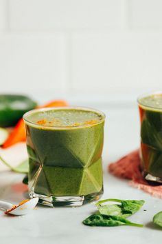 two glasses filled with green smoothie sitting on top of a table