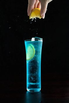 a hand is sprinkling lemon into a blue drink