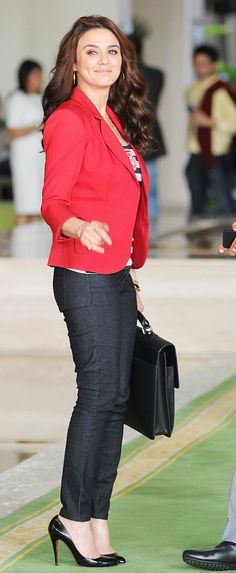 a woman in a red jacket and black pants holding a briefcase while standing next to a man