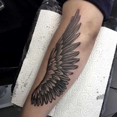 a black and white photo of a person with a tattoo on their arm that has an angel wing