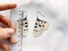 a pair of butterfly shaped earrings sitting on top of a white fur covered floor next to a ruler