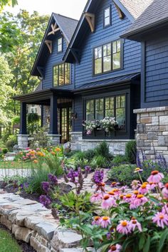 a blue house with lots of windows and flowers in the front yard, on a sunny day