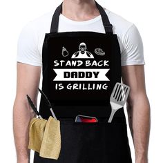 a man wearing an apron and holding a spatula in his hand with the words stand back daddy is grilling on it