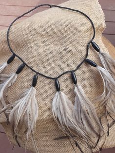 a black cord necklace with white feathers hanging from it's end on a piece of burlap