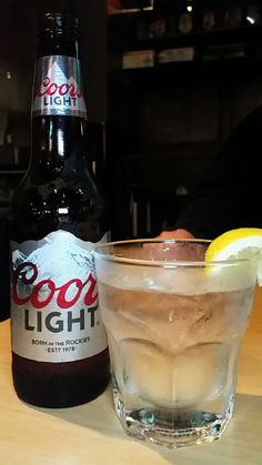 a close up of a glass on a table with a bottle and a lemon wedge