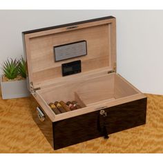 an open box with cigars inside on a wooden table next to a potted plant