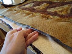 a hand is holding the edge of a piece of fabric on top of a table