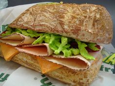 a sandwich with meat, lettuce and cheese on it sitting on top of a wrapper