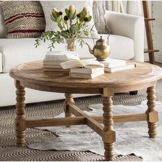 a coffee table with books and flowers on it in front of a white couches