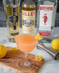 a glass filled with liquid next to bottles of alcohol and lemons on a cutting board