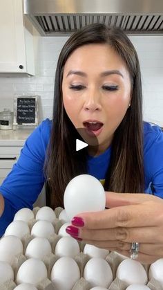 a woman holding an egg in her hand and looking at the eggs on the counter